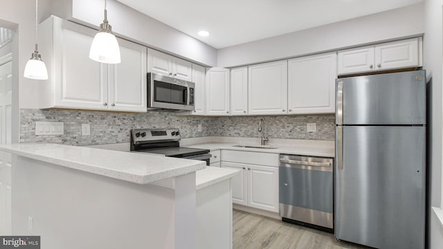 kitchen featuring a sink, stainless steel appliances, a peninsula, hanging light fixtures, and white cabinets
