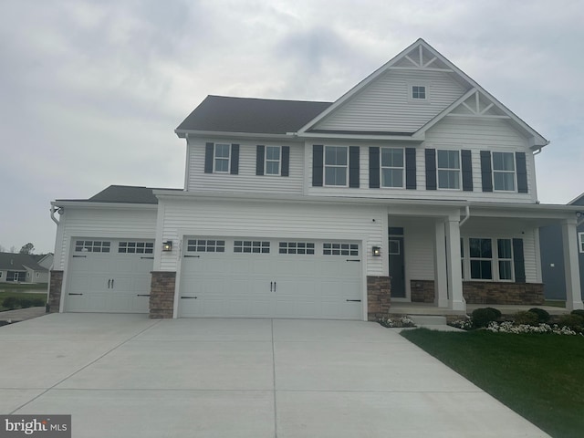 craftsman-style home with driveway, a garage, covered porch, and stone siding