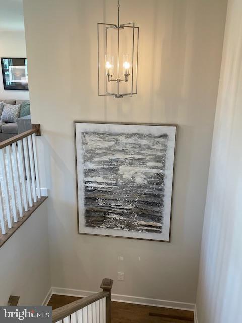 stairway with wood finished floors, a notable chandelier, and baseboards