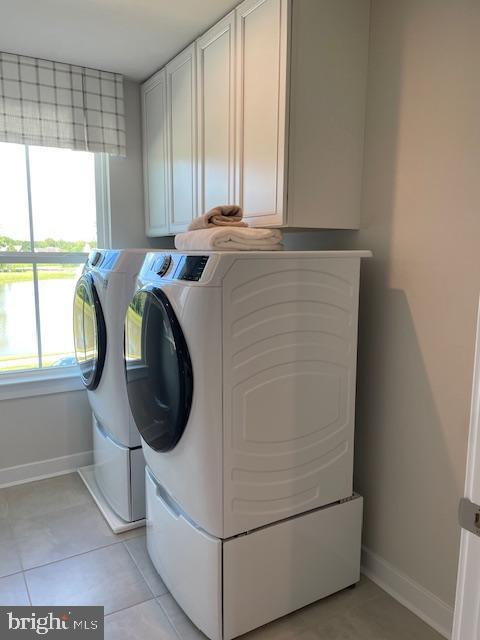 clothes washing area featuring light tile patterned flooring, cabinet space, washing machine and clothes dryer, and baseboards
