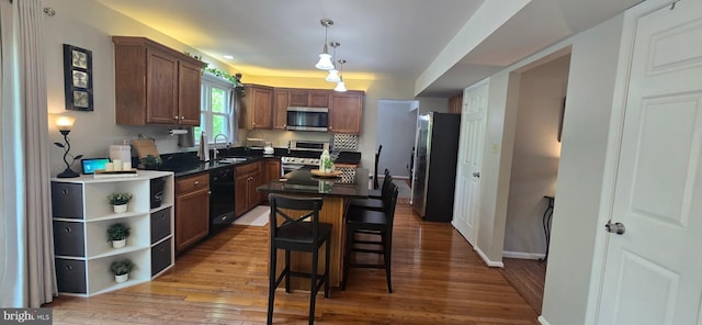 kitchen featuring light wood-style flooring, a sink, appliances with stainless steel finishes, dark countertops, and baseboards