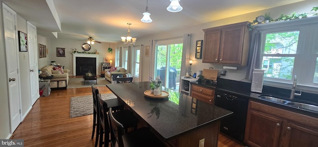 kitchen with dark wood finished floors, decorative light fixtures, black dishwasher, ceiling fan with notable chandelier, and a sink
