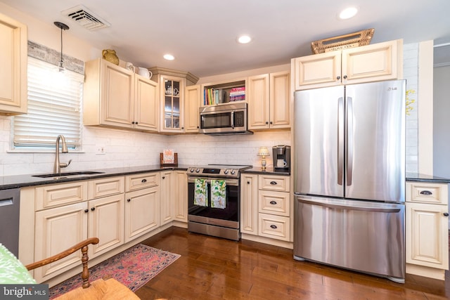 kitchen with a sink, stainless steel appliances, cream cabinetry, visible vents, and dark wood-style floors