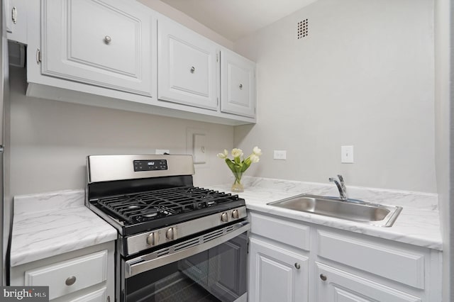 kitchen with gas stove, a sink, white cabinets, and visible vents