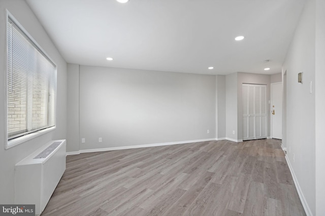 empty room featuring recessed lighting, radiator heating unit, baseboards, and light wood-style floors