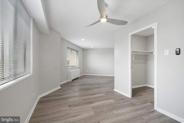 unfurnished bedroom with ceiling fan, a closet, baseboards, wood finished floors, and a walk in closet