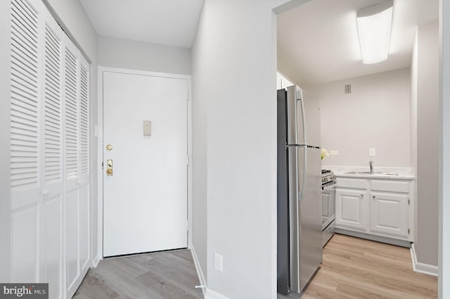 corridor with visible vents, light wood finished floors, and a sink