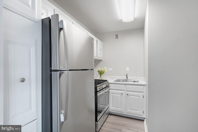kitchen featuring stainless steel appliances, light countertops, white cabinets, a sink, and light wood-type flooring