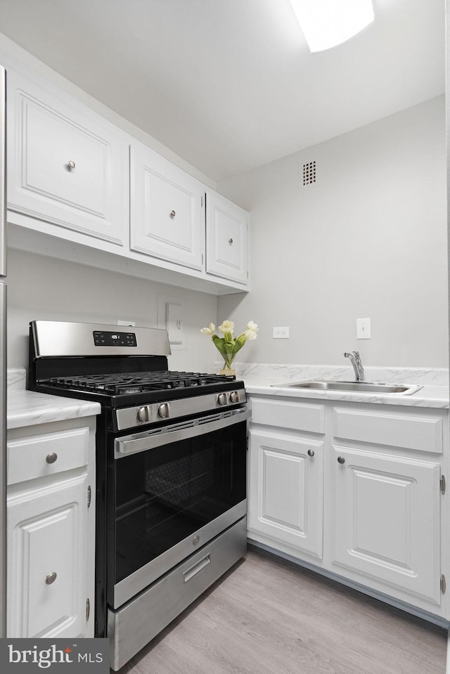 kitchen with a sink, stainless steel range with gas stovetop, white cabinetry, and light countertops