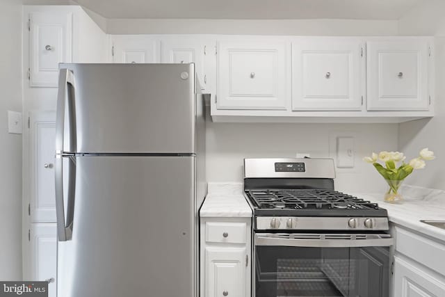 kitchen with stainless steel range with gas cooktop, white cabinetry, light stone counters, and freestanding refrigerator