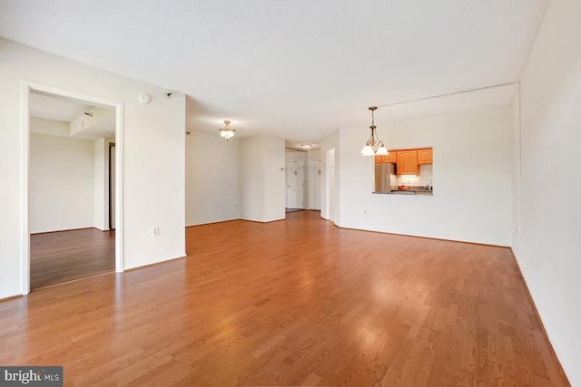 unfurnished living room with a notable chandelier and light wood finished floors