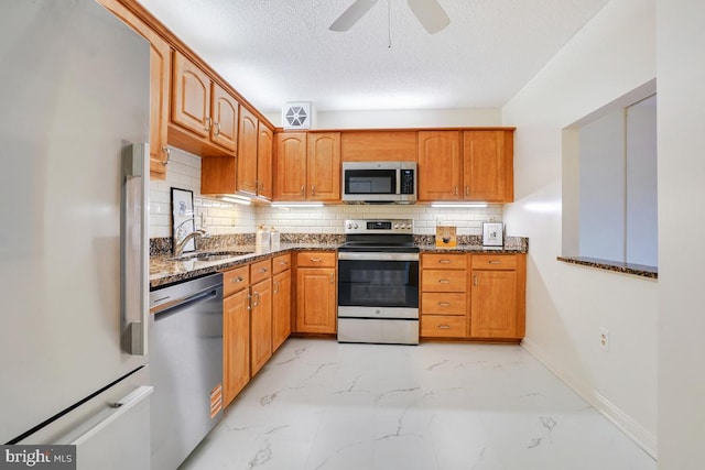 kitchen featuring decorative backsplash, marble finish floor, dark stone counters, a sink, and appliances with stainless steel finishes
