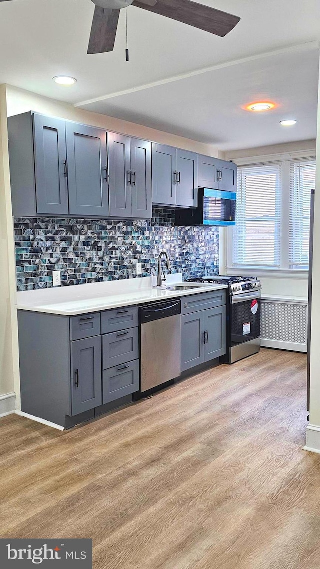 kitchen featuring light wood-type flooring, light countertops, tasteful backsplash, a ceiling fan, and stainless steel appliances