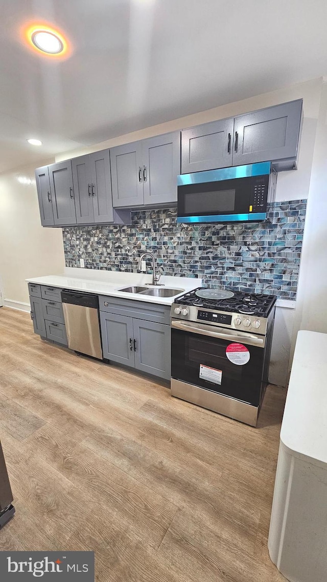 kitchen featuring backsplash, appliances with stainless steel finishes, light wood-type flooring, gray cabinetry, and a sink