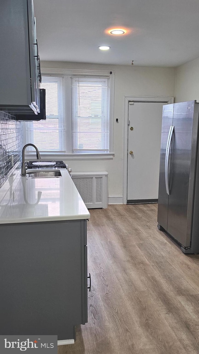 kitchen with freestanding refrigerator, radiator, light countertops, a sink, and light wood finished floors