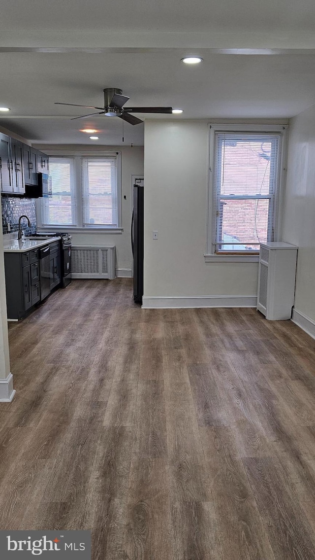 unfurnished living room with ceiling fan, wood finished floors, a sink, baseboards, and radiator