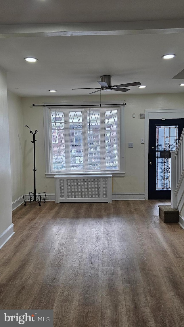 unfurnished living room featuring baseboards, ceiling fan, radiator heating unit, and wood finished floors