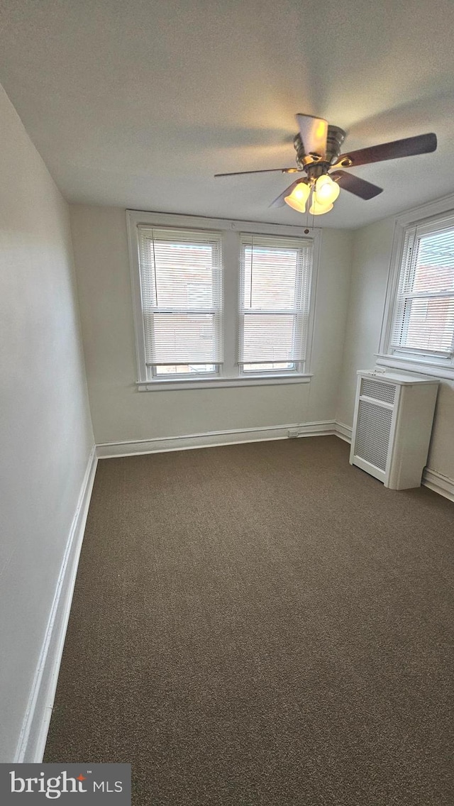 empty room featuring baseboards, a ceiling fan, dark carpet, and a textured ceiling