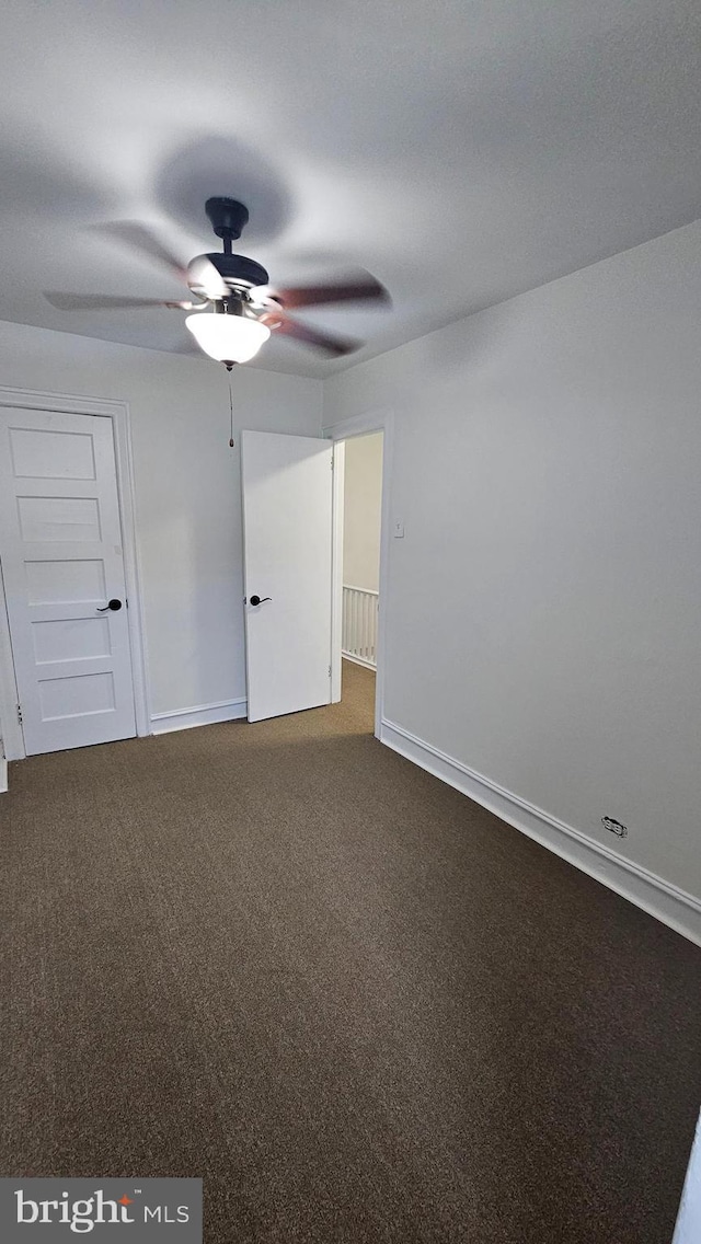unfurnished bedroom featuring baseboards, a ceiling fan, and dark colored carpet