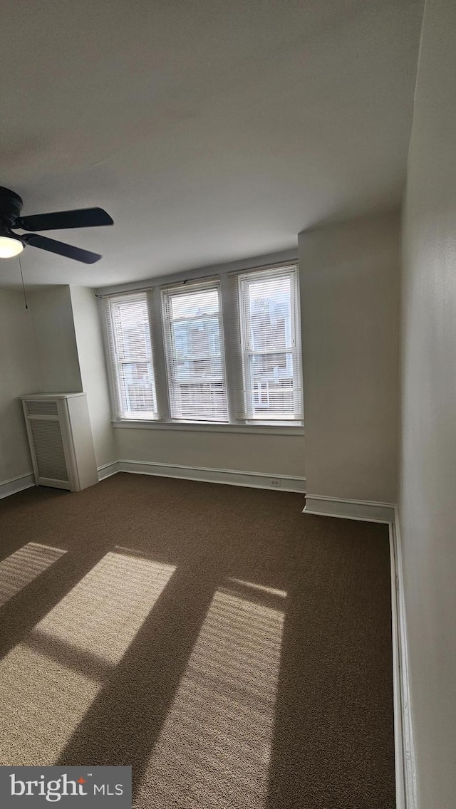carpeted spare room featuring a healthy amount of sunlight, baseboards, and ceiling fan