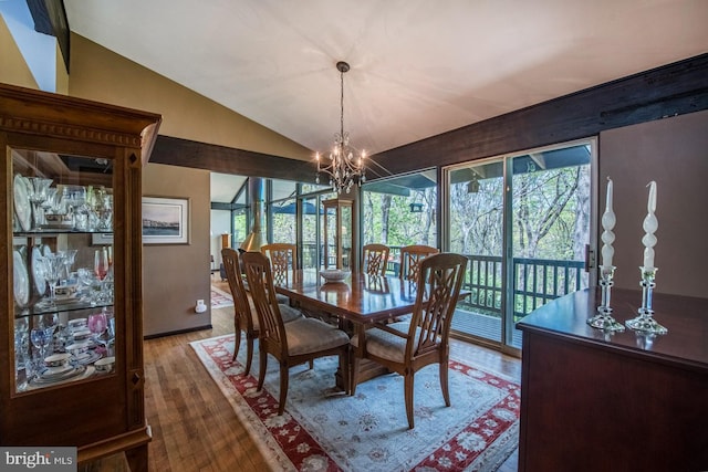 dining area with a notable chandelier, wood finished floors, and vaulted ceiling