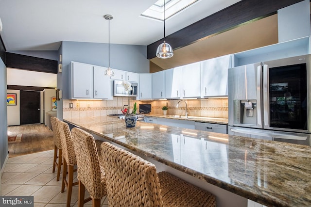 kitchen featuring white cabinets, appliances with stainless steel finishes, lofted ceiling with skylight, and tasteful backsplash