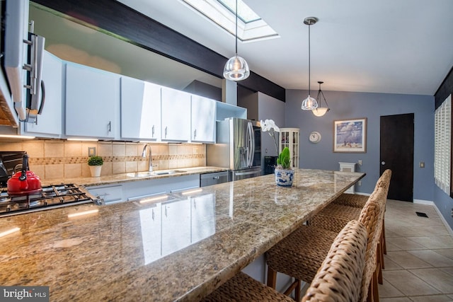 kitchen with a breakfast bar, a sink, vaulted ceiling with skylight, white cabinetry, and backsplash