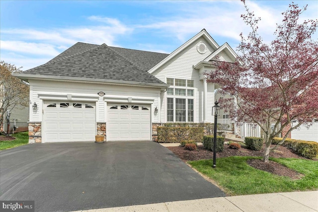 view of front facade featuring driveway, stone siding, a garage, and a shingled roof