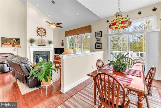 dining space with baseboards, a glass covered fireplace, wood finished floors, a ceiling fan, and high vaulted ceiling