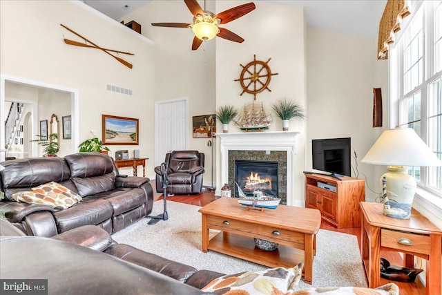 living room featuring wood finished floors, a high end fireplace, ceiling fan, visible vents, and a high ceiling