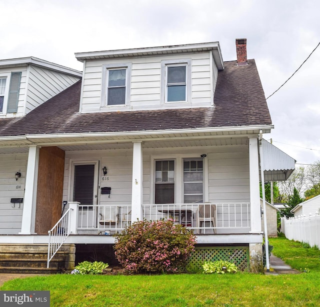 view of front of property featuring covered porch, a chimney, a shingled roof, and a front yard