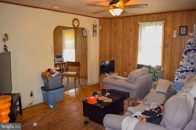 living area featuring arched walkways, wood finished floors, wood walls, ornamental molding, and ceiling fan