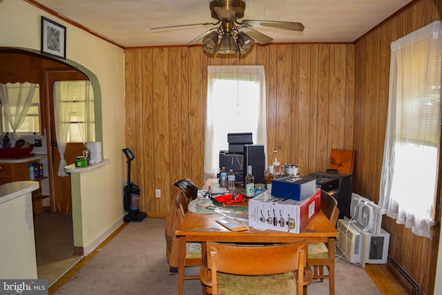 dining room with arched walkways, wood walls, ceiling fan, baseboards, and crown molding