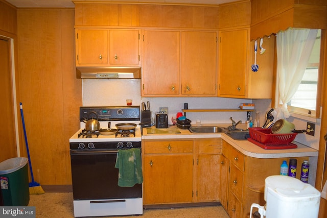 kitchen with a sink, light countertops, gas range, and under cabinet range hood