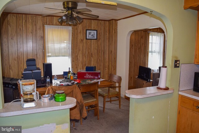 home office with arched walkways, ceiling fan, wooden walls, and carpet