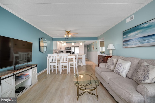 living room featuring ceiling fan, ornamental molding, light wood-style flooring, and visible vents