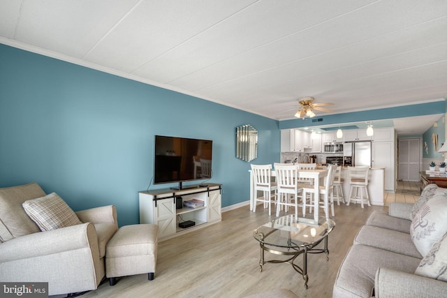 living room featuring a ceiling fan, ornamental molding, light wood-type flooring, and baseboards
