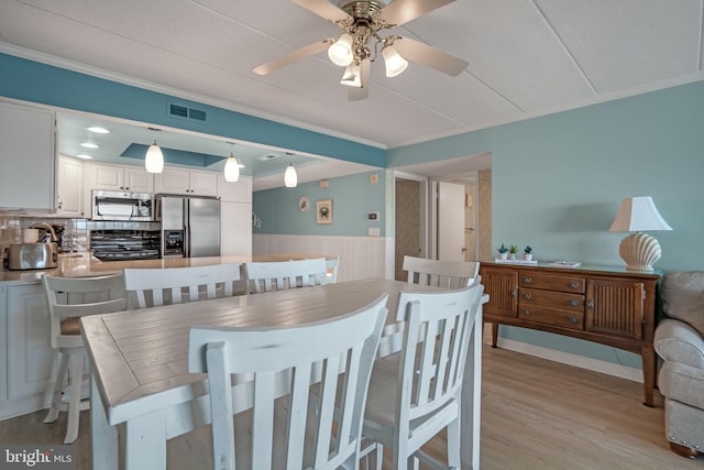 dining room with ceiling fan, wainscoting, and ornamental molding