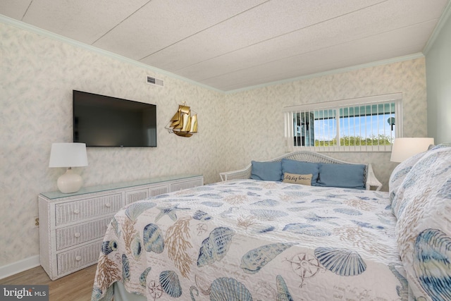 bedroom with ornamental molding, visible vents, wallpapered walls, and wood finished floors