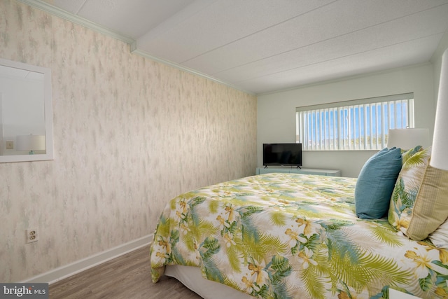 bedroom featuring crown molding, baseboards, wallpapered walls, and wood finished floors