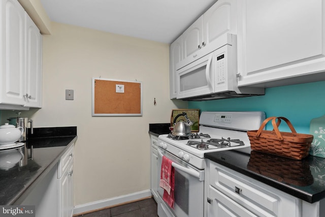 kitchen featuring dark tile patterned floors, white appliances, baseboards, dark countertops, and white cabinets