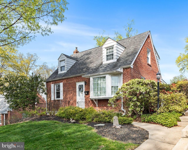 new england style home with brick siding, a front lawn, roof with shingles, and a chimney