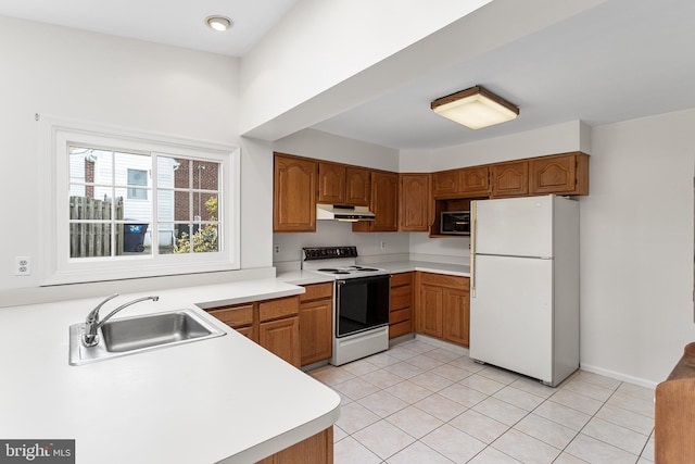 kitchen featuring brown cabinetry, freestanding refrigerator, electric stove, under cabinet range hood, and a sink