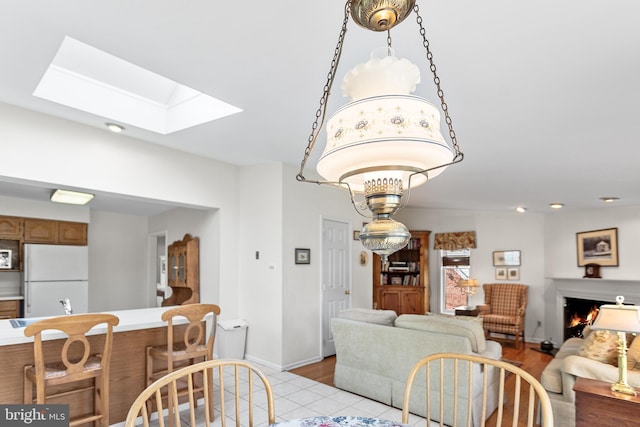 dining space with a skylight, baseboards, light wood-type flooring, and a warm lit fireplace