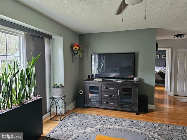 living room featuring a textured ceiling, ceiling fan, light wood-type flooring, and baseboards