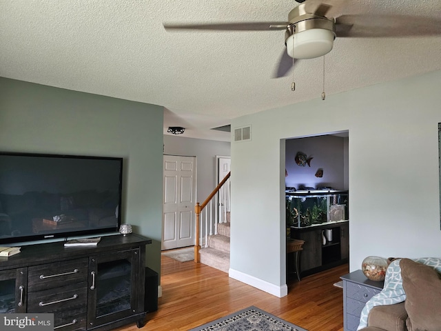 living area with a textured ceiling, stairway, ceiling fan, visible vents, and light wood finished floors