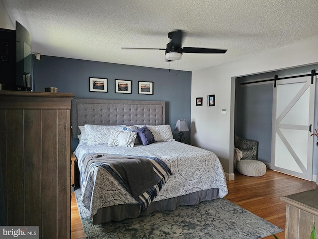bedroom featuring a barn door, a textured ceiling, a ceiling fan, and wood finished floors
