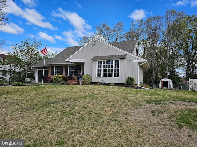 view of front facade with roof with shingles, a front yard, a storage shed, and an outdoor structure