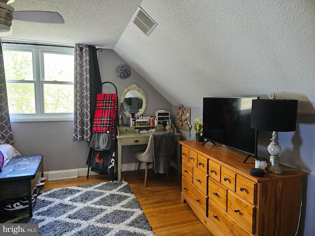 bedroom with lofted ceiling, a textured ceiling, visible vents, and wood finished floors