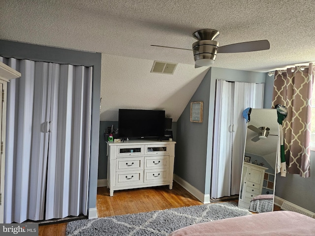 bedroom with visible vents, light wood-style flooring, vaulted ceiling, baseboards, and a textured ceiling
